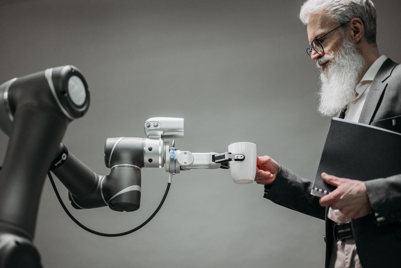 about-01 An elderly man receives a cup from a robotic arm in a modern office setting.